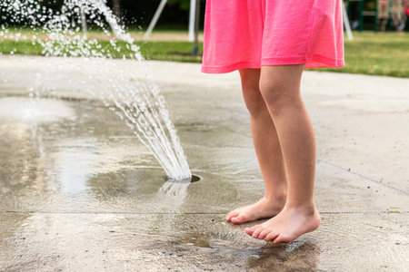 Little child playing with water and toys at splash pad in the local public park during hot summer day. Small beautiful girl in pink dress having fun at fountain playground.の写真素材