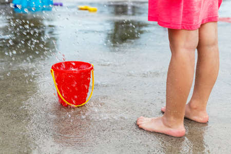 Little child playing with water and toys at splash pad in the local public park during hot summer day. Small beautiful girl in pink dress having fun at fountain playground.の写真素材