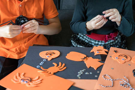 Halloween kids craft preparations. Little children doing crafts at home. Boy and girl wearing black and orange clothes, sitting at the table, maiking spiders.の写真素材