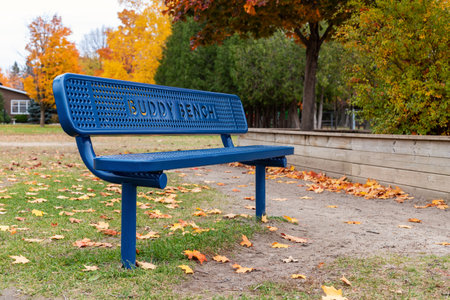 Ottawa, Canada - October 14, 2021: Blue buddy bench in local public park at schoolyard in fall. Autumn trees with colorful leavesのeditorial素材