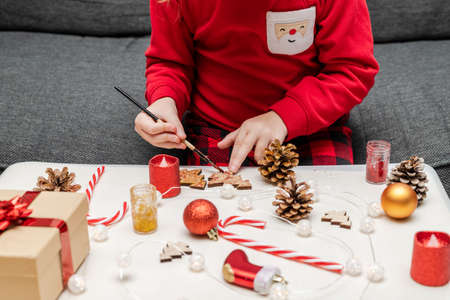Christmas kids craft activities . Little child painting pine cones and wooden Christmas tree decorations at home. Holiday DIY for children.の写真素材