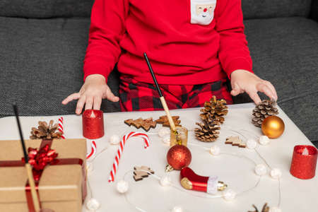 Christmas craft activities for kids at home. Little child painting pine cones and wooden Christmas tree decorations sitting at table. Holiday DIY concept for children.の写真素材