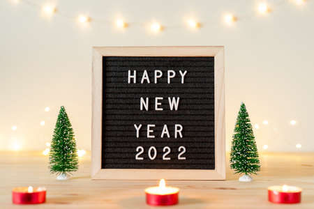 Happy new year 2022 greetings on letter board with holiday lights, candles and small decorative Christmas trees on wooden table.の写真素材