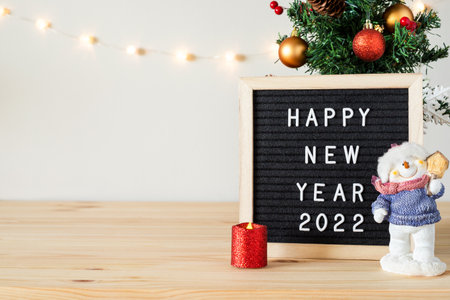 Happy new year 2022 greetings on black felt letter board and Christmas tree with decorations, toy...
