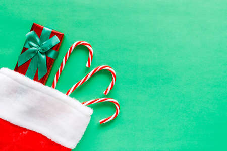 Christmas stocking with gift and candy canes on green background with copy space for text. Flat lay composition of holiday decorations.の写真素材