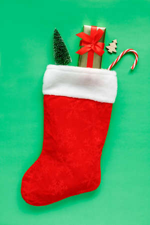 Christmas stocking with gift box, toy trees and candy cane on green background with copy space for text. Flat lay composition of holiday decorations.の写真素材