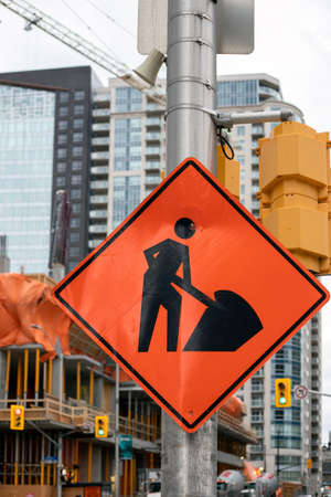 Construction orange sign near construction site against tall buildings and skyの写真素材