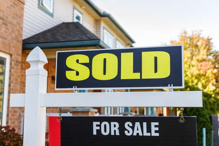 Sold yellow and black sign close-up in front of a house in a residential neighborhoodの写真素材