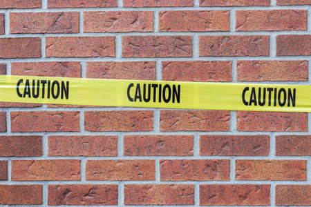 Caution yellow tape closeup against red brick wall.の写真素材