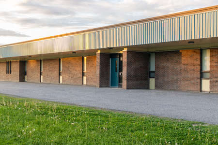 School building exterior and schoolyard with green grass in front on a sunny evening. Elementary public school entrance.の写真素材