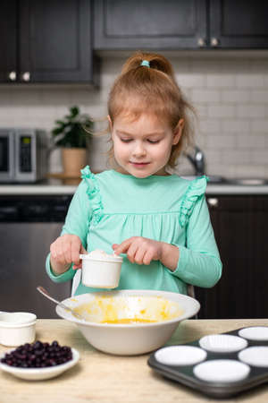 Little smiling cute girl mixing ingredients for baking homemade muffins. Child cooking at home . Small kid having fun in kitchen, learning to cookの写真素材