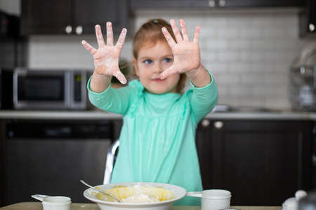 Little girl having fun cooking in kitchen. Small happy child mixing dough, showing hands with flour.の写真素材