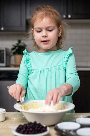Child cooking muffins in the kitchen. Ingredients for baking on table. Little girl making dough, learning to cook at home.の写真素材