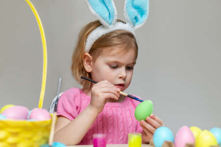 Little girl in Easter bunny ears painting colored eggs. Holiday celebration at home and crafts for children.の写真素材