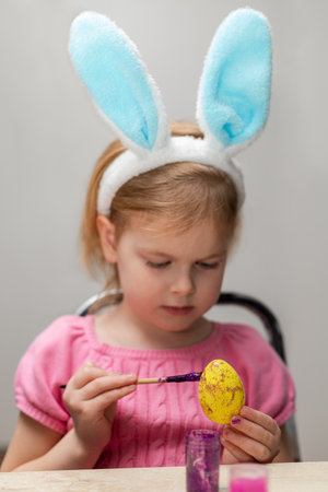 Little girl in Easter bunny eaLittle girl in Easter bunny ears painting colored eggs. Easter family...