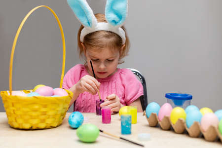 Little child in bunny ears painting Easter eggs. Small kid making holiday decorations, doing craftsの写真素材