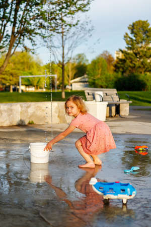 Happy child playing with toys and water in park splash pad. Girl at playground in summer barefootの写真素材