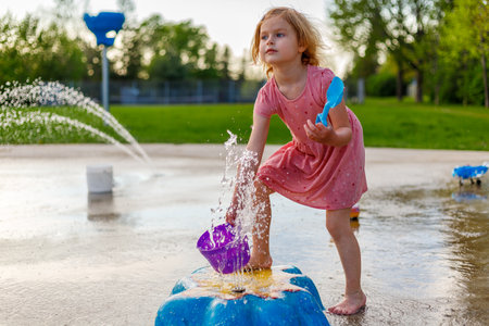 Small child playing at splash pad playground in summer. Water park with fountains for children. Summertime activities for kidsの写真素材