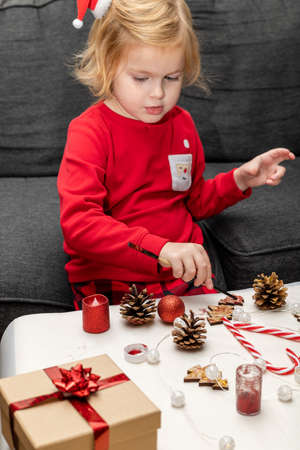 Christmas kids craft activities at home. Little child painting pine cones and wooden Christmas tree decorations at home. Holiday DIY concept for children.の写真素材