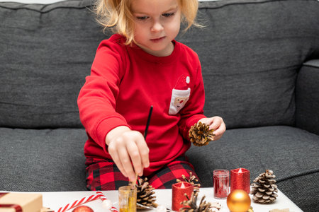 Christmas kids craft activities at home. Little child painting pine cones and wooden Christmas tree decorations at home. Holiday DIY concept for children.の写真素材