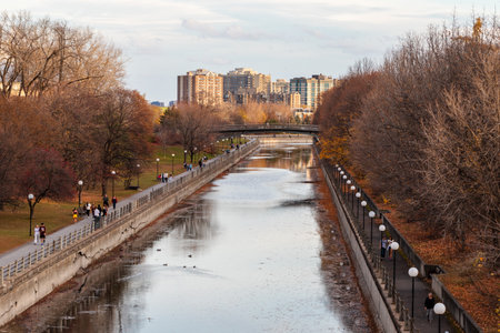 Ottawa, Canada - November 5, 2022: Rideau Canal in autumn season in park with pathway, bike lane with walking people and buildingsのeditorial素材