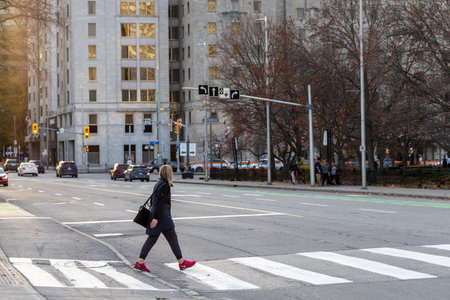 Ottawa, Canada - November 5, 2022: Woman crossing street in downtown. Cityscape with crosswalk and walking peopleのeditorial素材