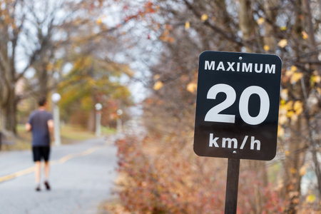 Speed limit sign, 20 kilometers per hour for bicycle lanes. Man jogging in park.の写真素材