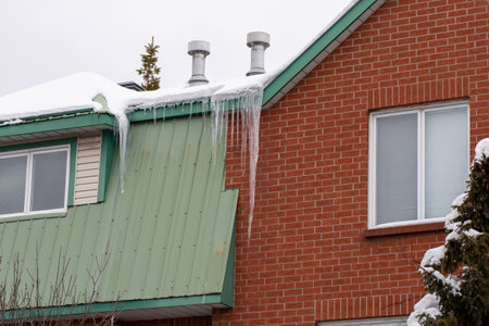 Icicles hanging from roof of the house covered with snow in winter
