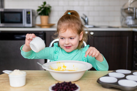 Little smiling girl making dough in kitchen. Small happy child cooking. Kid baking homemade muffins with berries, learning to cook.の写真素材