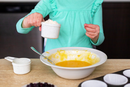 Little girl making dough in kitchen. Small child cooking. Kid making homemade muffins with berries, learning to cook.の写真素材