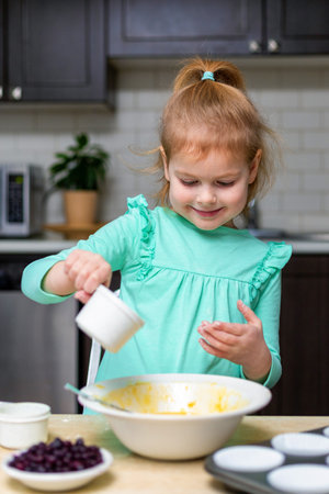 Little smiling girl making dough in kitchen. Small happy child cooking. Kid making homemade muffins with berries, learning to cook.の写真素材