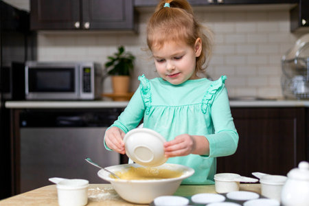 Small happy child cooking. Kid making homemade muffins, mixing ingridients, learning to cook. Little smiling girl making dough in kitchen.の写真素材