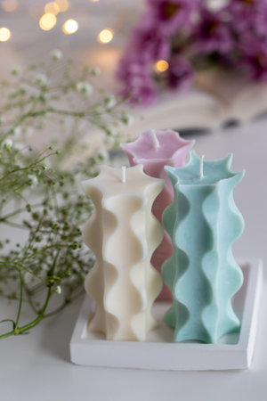 Three candles on a table with a book, flowers and lights in background. Home decor. Cozy interior.の写真素材