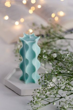 Blue candle on a table with a book, flowers and lights in background. Cozy interior.の写真素材