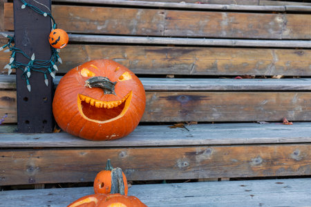 Fall decorations for Halloween holiday. Carved pumpkin on outdoor wooden stairs. Copy spaceの写真素材