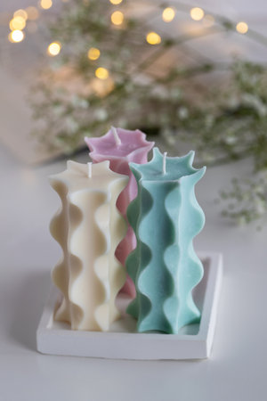 Three soy candles on a table with a book, flowers and lights in background. Home decor. Cozy interior.の写真素材