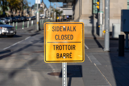 Orange sidewalk closed sign in English and French on road in downtown street in Ottawa, Canadaの写真素材