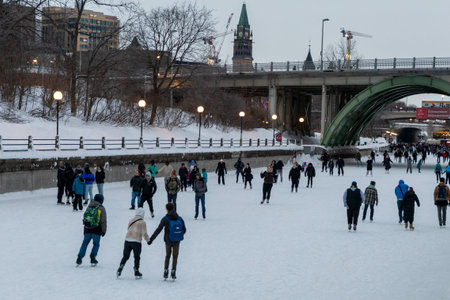 Ottawa, Canada - February 8, 2025: Ice skating rink on Rideau Canal in winter. Parliament building in downtown in evening.のeditorial素材