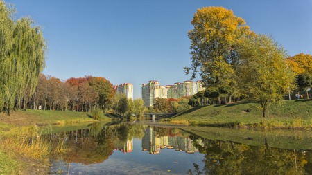 Beautiful fall colors reflect off a pond. Autumn park with high building.の写真素材