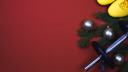 Red dumbbells, yellow sneakers and branches of Christmas tree with ornament on the red backgroundの写真素材
