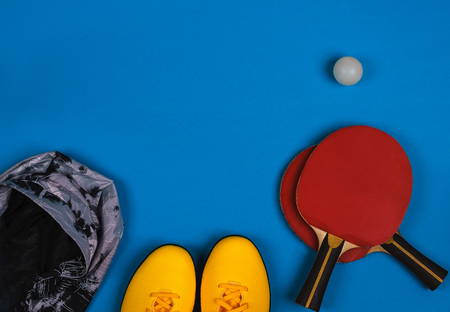 Top view on the sport composition with yellow sneakers, grey jacket, red tennis rocket with ball on the bright blue backgroundの写真素材