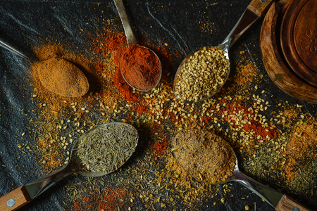 Oriental spices laid out in spoons and scattered on the black metallic tray in Asian styleの写真素材