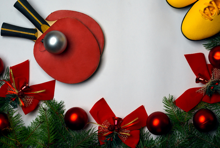 Christmas and New Year background with green branches of fir tree red glass balls and red bows bells on white background and yellow sneakers sport shoes and two red tennis rackets. View from above. Copy space. Fitness, healthy and active lifestyles greeting card concept.の写真素材