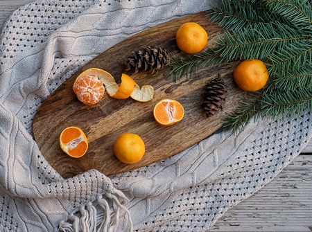 Sweet tangerines, fir tree brunches, pine cones on wooden kitchen board in rustic style on wooden background and gray knitted plaid. Christmas food decorations. Table setting. Flat lay copy space.の写真素材