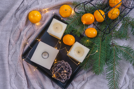 Christmas background. Flat lay to candles, orange tangerines, pine cone fir on black tray fairy lights on gray plaid background. Christmas decorations inspiration, layout idea. Top view copy spaceの写真素材