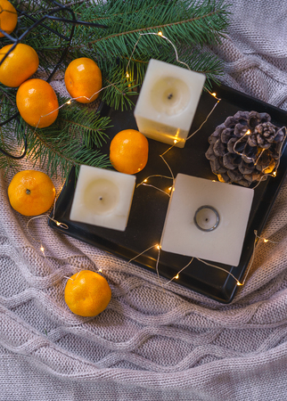 Christmas background. Flat lay to candles, orange tangerines, pine cone fir on black tray fairy lights on gray plaid background. Christmas decorations inspiration, layout idea. Top view copy spaceの写真素材