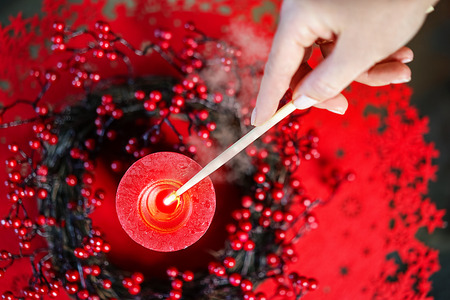 Burning candle from the hands of woman lighting a Christmas candle with red decoration, hand and smoke on the background. Chrismas New Year layout concept. Top view, flat lay. Lifestyleの写真素材