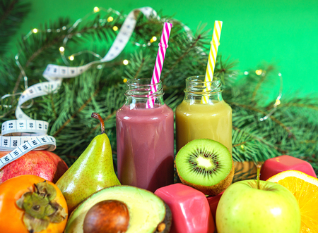Christmas healthy concept fruits and vegetables. Keto diet food ingredients bottles smoothies acai berry measuring tape dumbbell kiwi avocado pomegranate orange pear fir branches green background.の写真素材