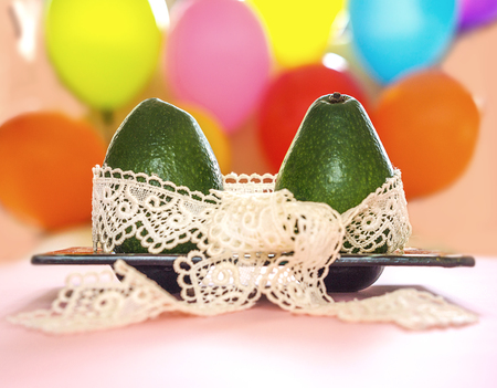 Green avocado with white lace ribbon on colorful balloons background. Healthy care and relationship symbol. Minimal style romance love creative concept Valentines day, wedding betrothal anniversaryの写真素材