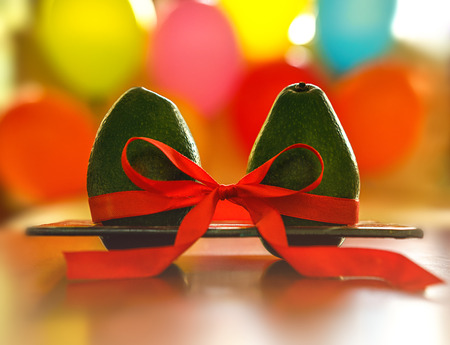 Green avocado with red silk ribbon on colorful balloons background. Healthy care and relationship symbol. Minimal style romance love creative concept Valentines day, wedding betrothal anniversaryの写真素材